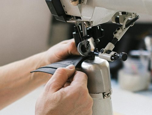 Close-up shot of hands crafting leather on a sewing machine, showcasing artisanal skills.